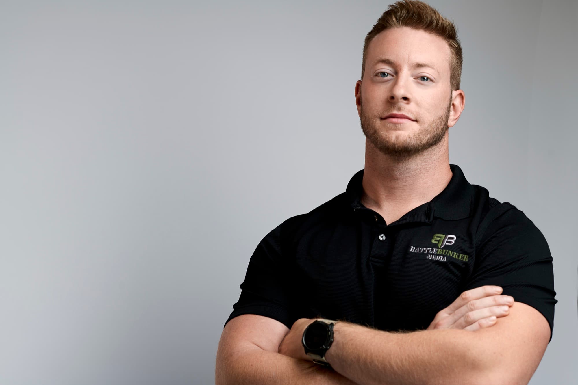 Austen Alexander standing with arms crossed in a black Battle Bunker Media polo shirt