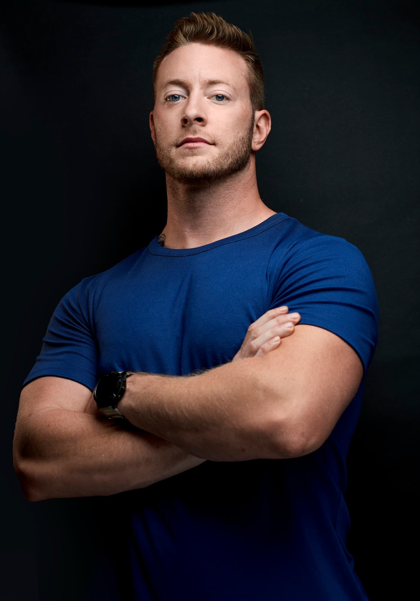 Austen Alexander in a navy blue t-shirt with arms crossed against a dark background